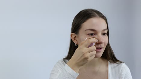 european caucasian young woman applying makeup foundation with sponge isolated on grey background