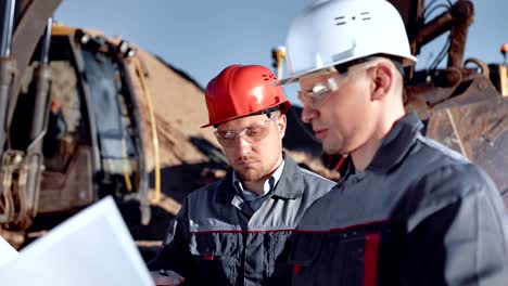 male foreman and worker in helmet and glasses discussing construction plan looking on drawing