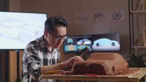 el diseñador automotriz asiático está mirando una tableta y revisando su escultura de arcilla de coche en el estudio