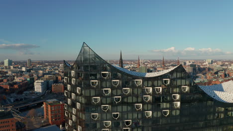 Close-up-aerial-view-of-modern-Elbphilharmonie-concert-hall-building-rooftop-with-reveal-of-famous-Hamburg-churches-in-the-background