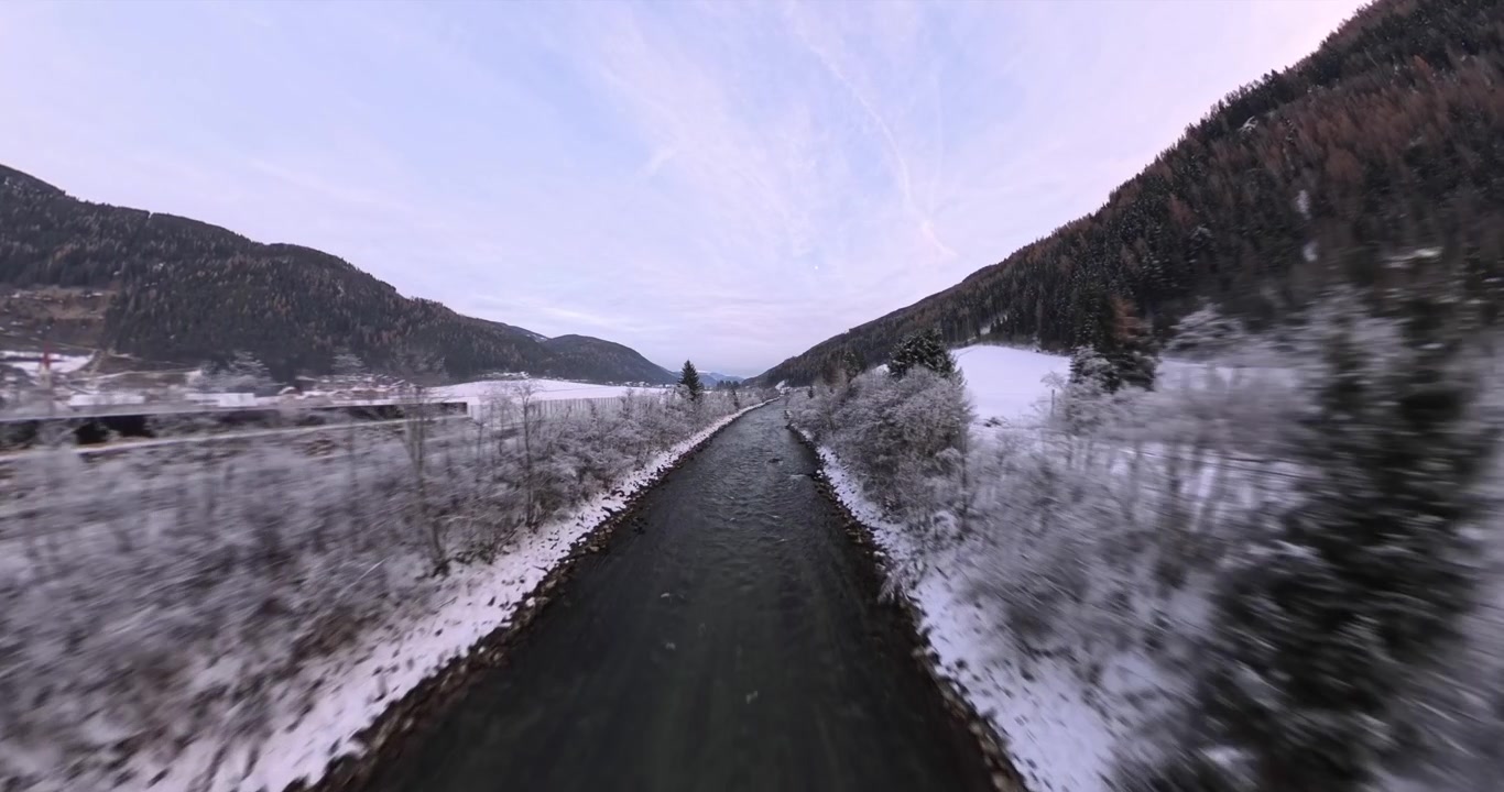 Vista drone che vola bassa lungo un fiume alpino con sponde innevate e foresta in Alto Adige, Italia. Avanzamento aereo a bassa quota.