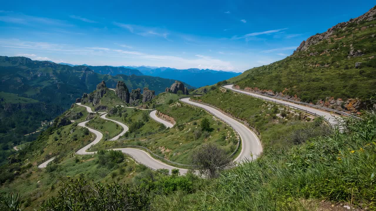 Starting camera capturing winding mountain road on hillside, with guardrails and shrubs