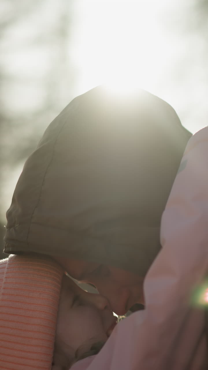 una niña con una gorra rosa y una chaqueta llevada por un hombre con una chaqueta marrón, mientras tocan sus frentes juntos afectuosamente