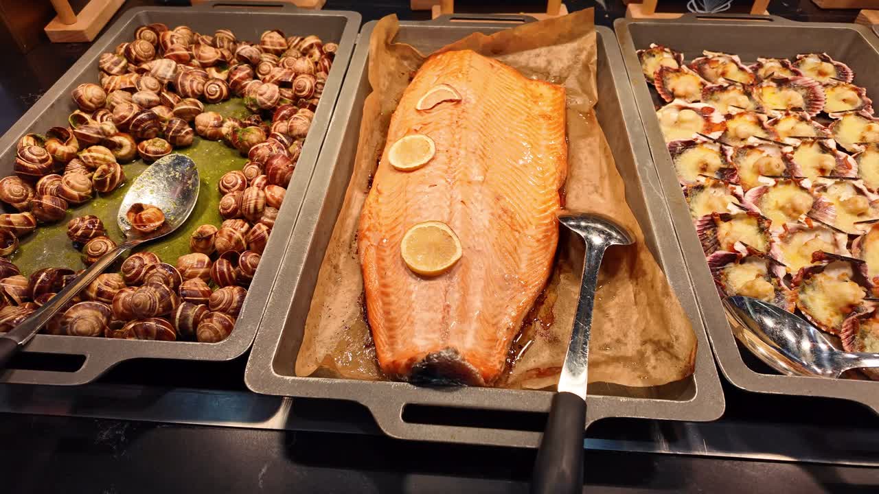 Esposizione di buffet gourmet con un lato intero di salmone arrosto con limone, capesante gratinate nei loro gusci ed escargot tradizionali francesi. Deliziosa varietà di frutti di mare pronta per essere servita