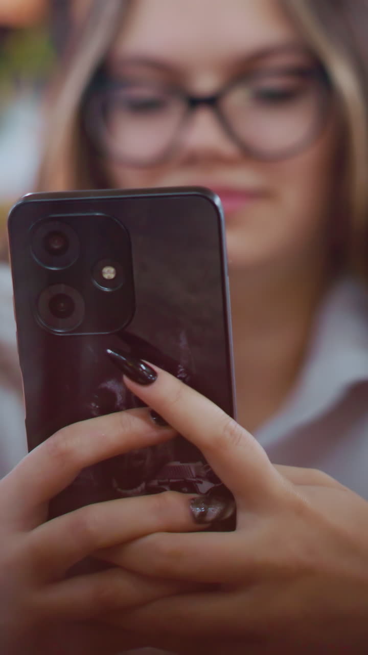 검은색 화된 손을 가진 여성이 스마트폰을 사용하고 있으며, 그녀의 얼굴이 약간 흐릿하고 활기찬 배경 보케가 있습니다.