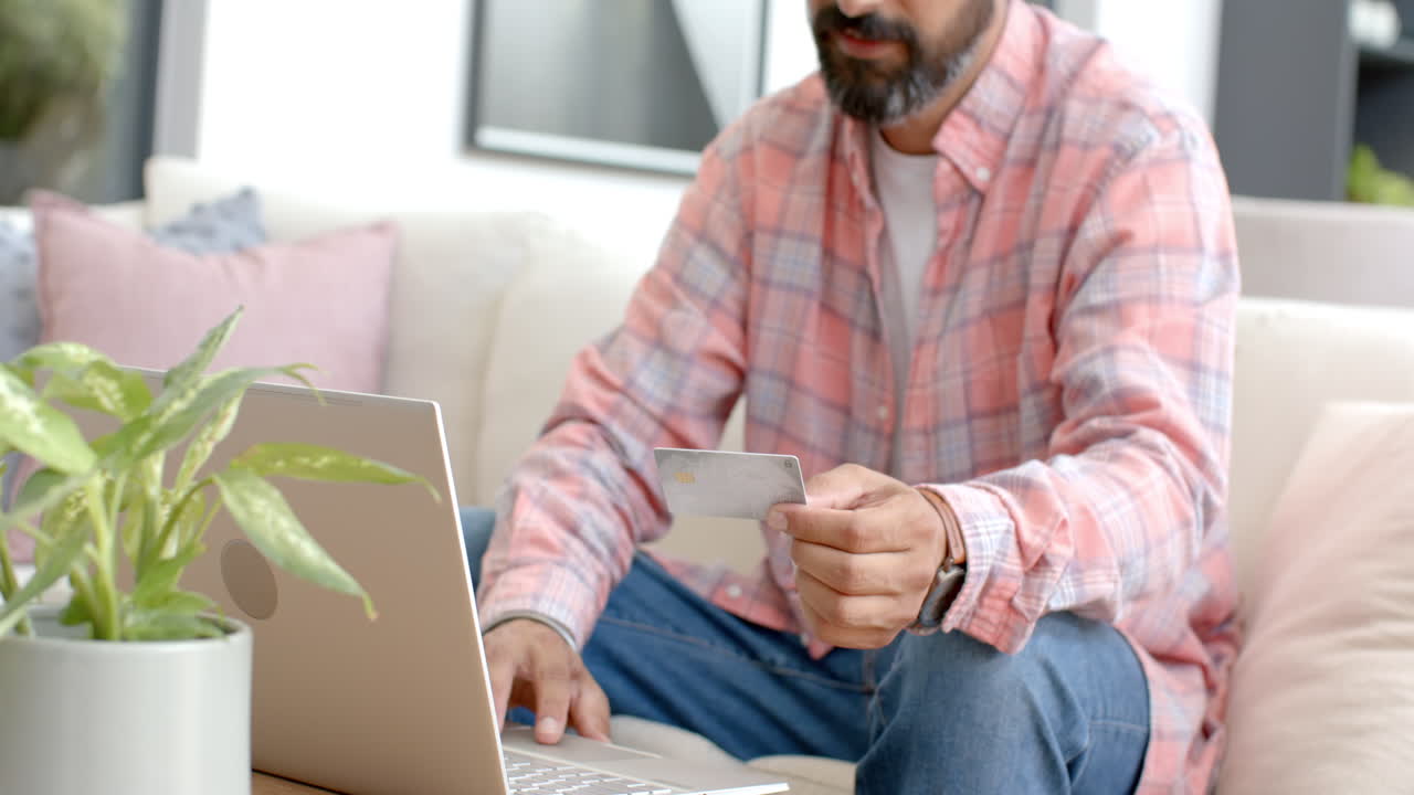 Using credit card, man shopping online with laptop on couch at home