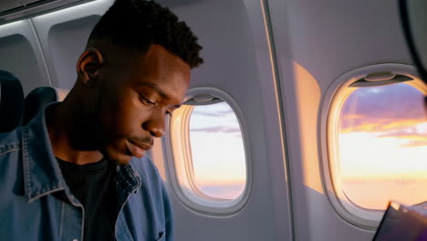 man focused on device during airplane sunset flight