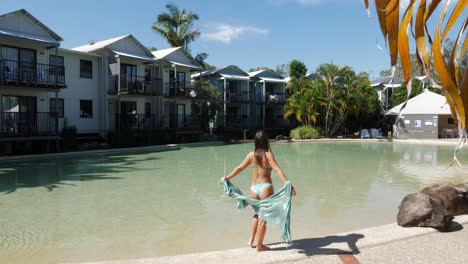 female model stands facing the swimming pool during sunny day at holiday resort in queensland, australia