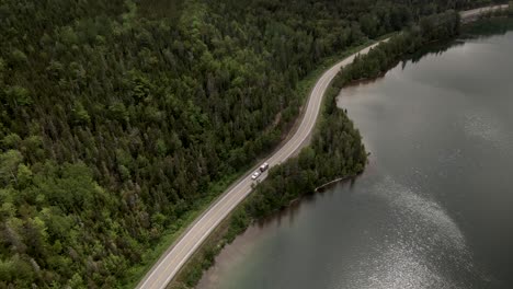 Cars-Travelling-On-The-Seaside-Road-By-The-Calm-Waters-Of-Saint-Lawrence-And-Lush-Green-Forest-In-Gaspe-Peninsula,-Quebec,-Canada