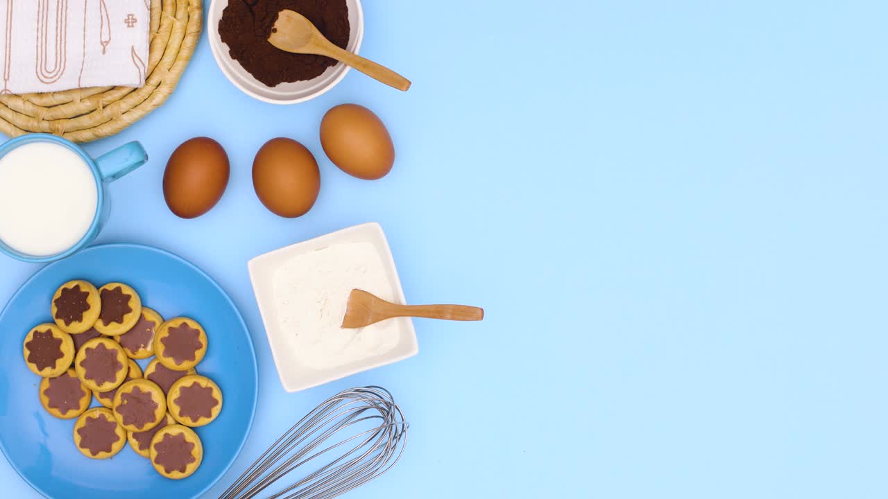 los ingredientes, la harina, los huevos, el cacao y las galletas en el plato aparecen en el lado izquierdo del tema azul.