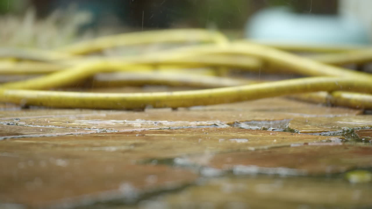 Yellow garden hose on tiles during rainfall
