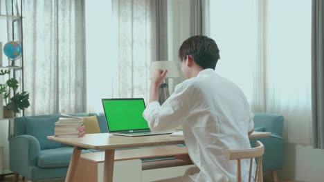 hind view of asian man student celebrating while looking at green screen computer at home