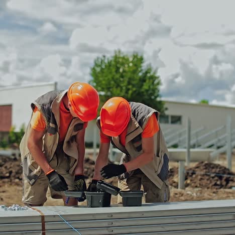 solar plant construction. two workers in orange helmets prepare instruments for building solar panels. engineers installing metal basis for future solar power plant.