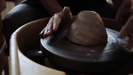 the hands of a young male potter are kneading clay lying on a potter's wheel