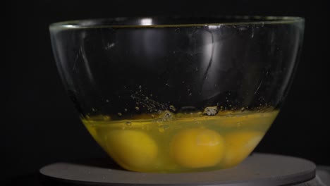 egg falling into a bowl with eggs on a black background in slow motion