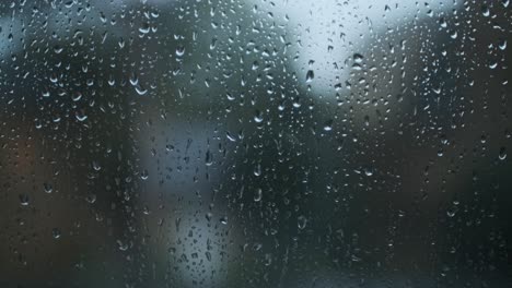 Raindrops-falling-down-glass-window-trees-in-background-close-up-dark