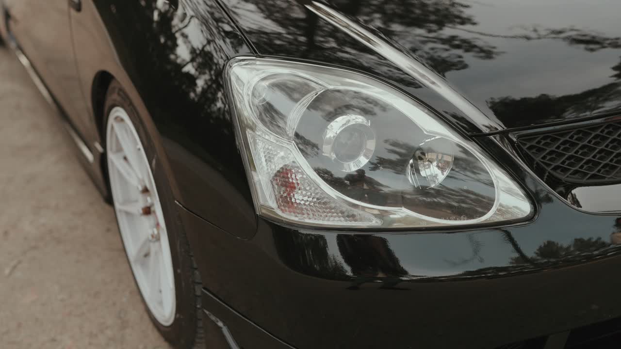 Closeup of black car front headlight and white wheel rim on pavement