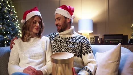 retrato de una hermosa esposa alegre que recibe una caja de regalo de navidad de su amado esposo en casa