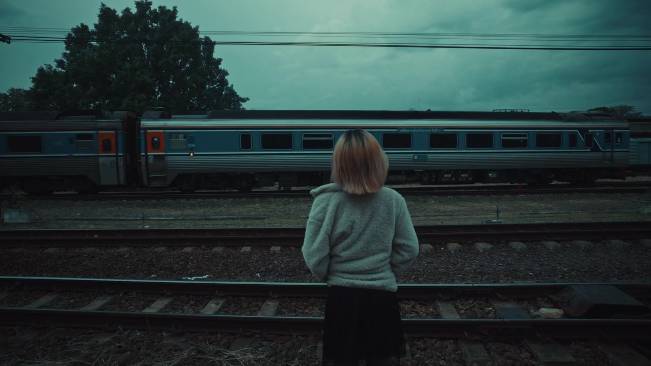 Woman Standing by Train Tracks as a Passenger Train Passes