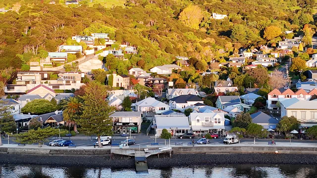 Drone footage captures Akaroa's scenic waterfront and hillside homes during golden hour, highlighting vibrant colors and tranquil waters