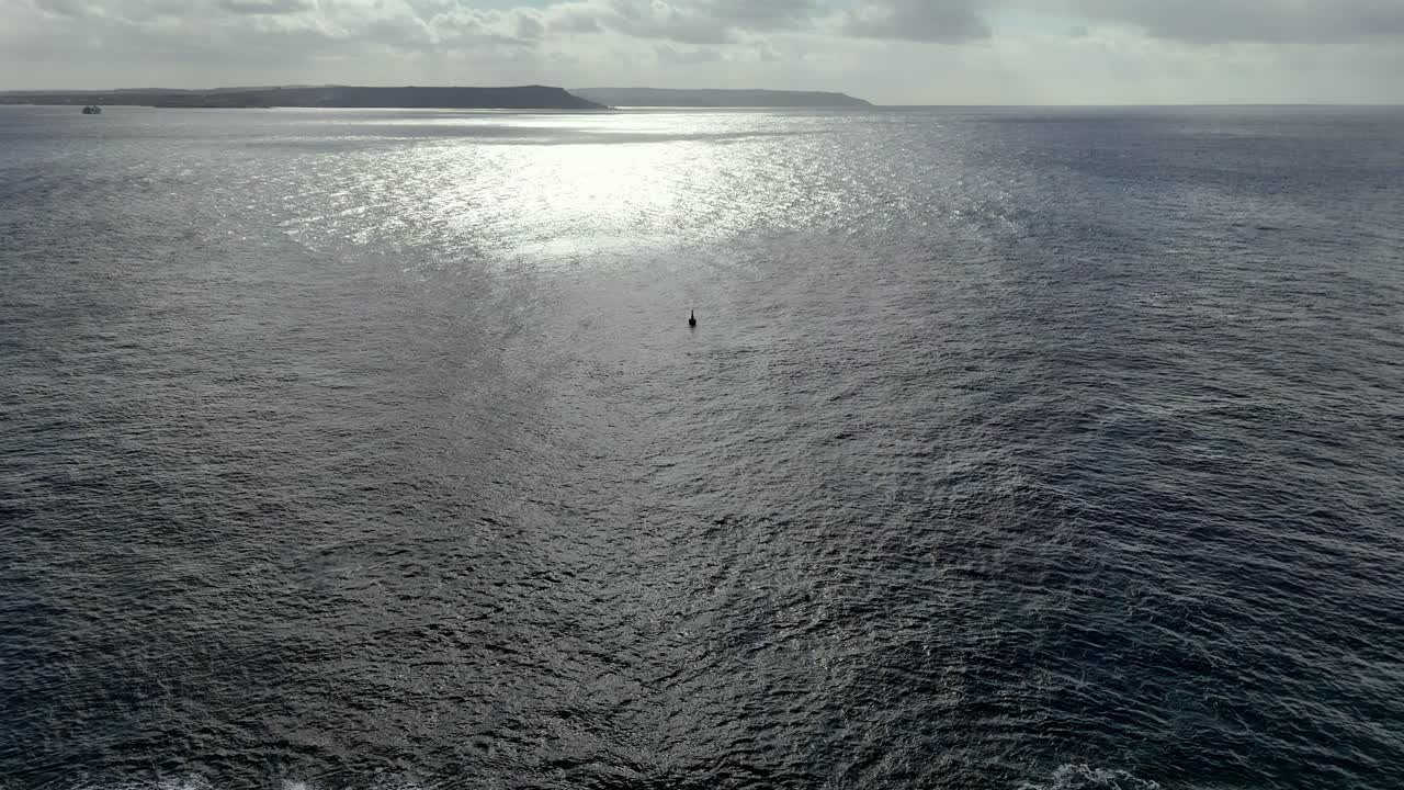 Spettacolare vista aerea del sole che brilla sull'immenso orizzonte del Mediterraneo vicino alla frastagliata costa maltese durante un luminoso pomeriggio, con scintillanti riflessi argentati e profonde tonalità blu dell'oceano