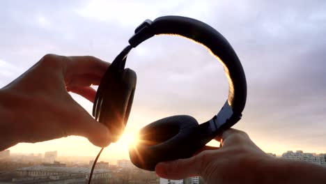 mans hand hold headphones at sunset city background. lens flare effect