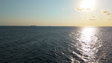 Grandes-Barcos-Navegan-En-El-Horizonte-Del-Océano-Mientras-El-Agua-Brilla-Por-La-Luz-Del-Sol,-Aérea