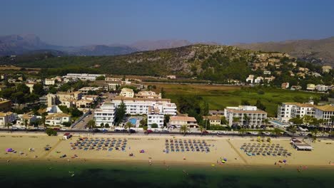 Playa-Del-Port-De-Pollenca-Mit-Sonnenanbetern-Und-Sonnenschirmen,-Mallorca,-Spanien,-An-Einem-Sonnigen-Tag,-Luftaufnahme