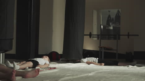 Children have break in sports center after training. Tired little kids lie calmly on floor in fighting gym after active workout slow motion. Small fighters