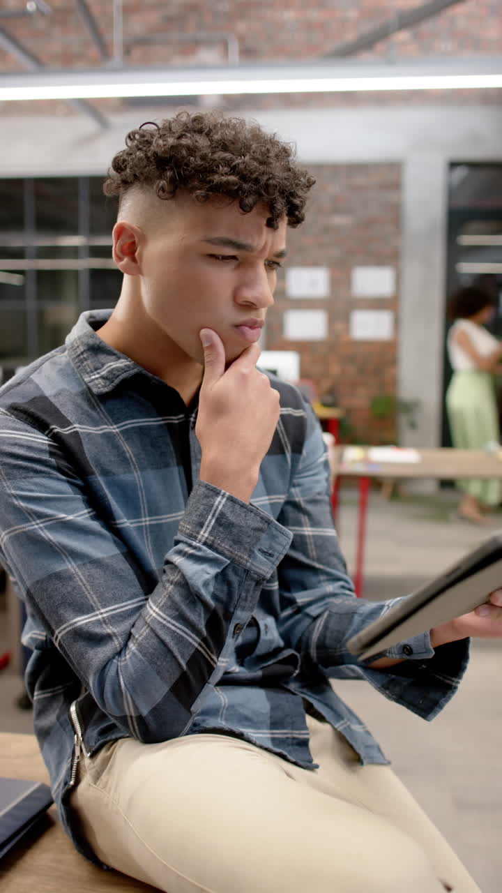 Vertical video of biracial businessman using tablet in office in slow motion