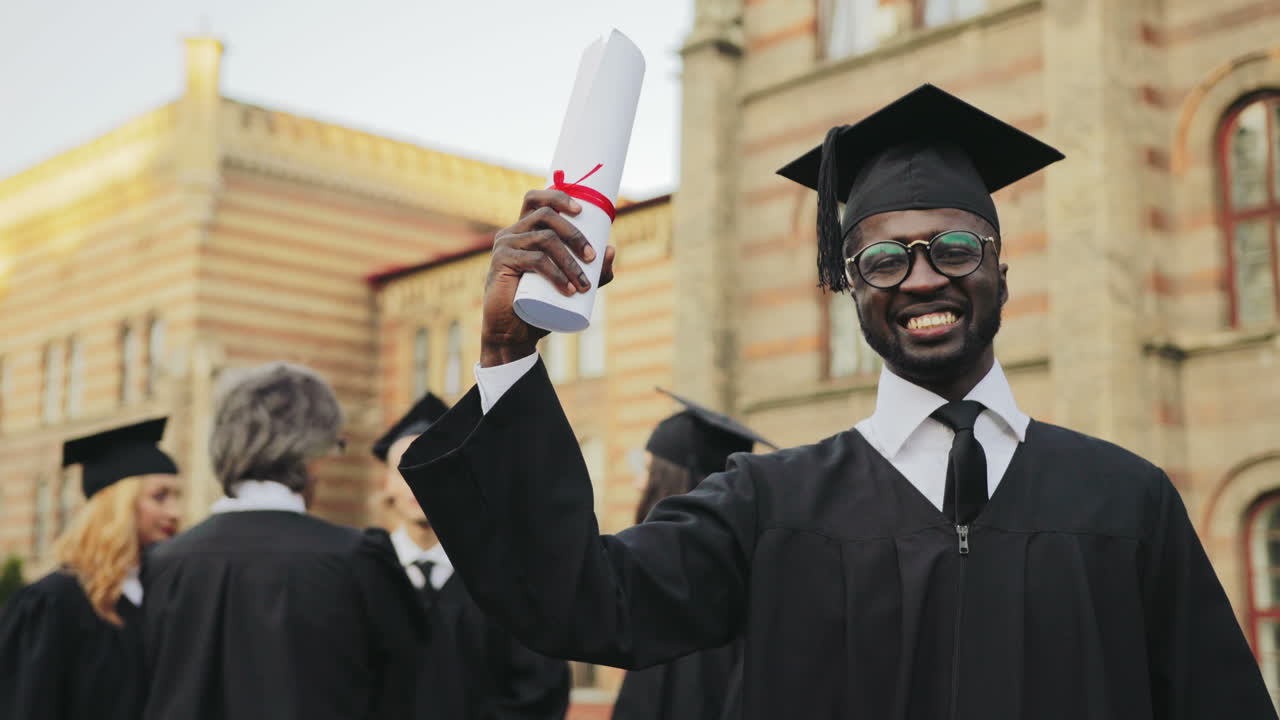 Portrait of an African American happy young graduated man posing to the camera and showing his diploma in front of the University
