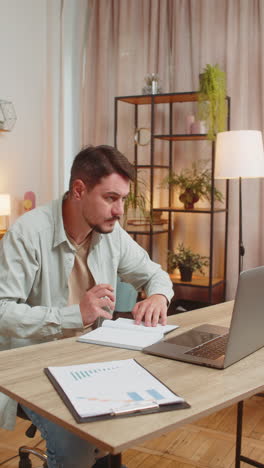 joven escribiendo notas mientras asiste a una reunión de oficina en línea en una computadora portátil en el escritorio de la oficina en casa