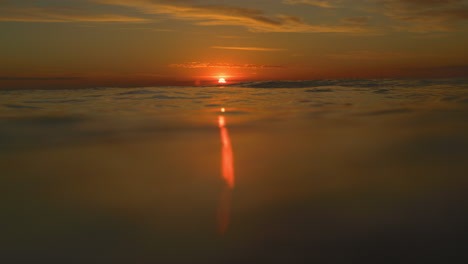 superficie del agua del océano con bola roja de puesta de sol que arroja luz en un rayo singular al anochecer