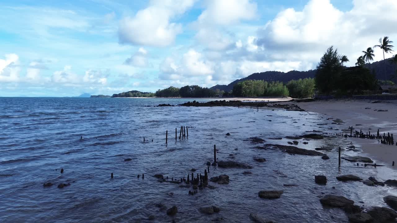 Pemandangan udara dari drone di Pantai Panjang berpasir di Koh Lanta yang menampilkan air berwarna pirus, ombak yang tenang, dan garis pantai tropis yang lebar dikelilingi oleh tanaman hijau subur dan suasana pulau yang tenang