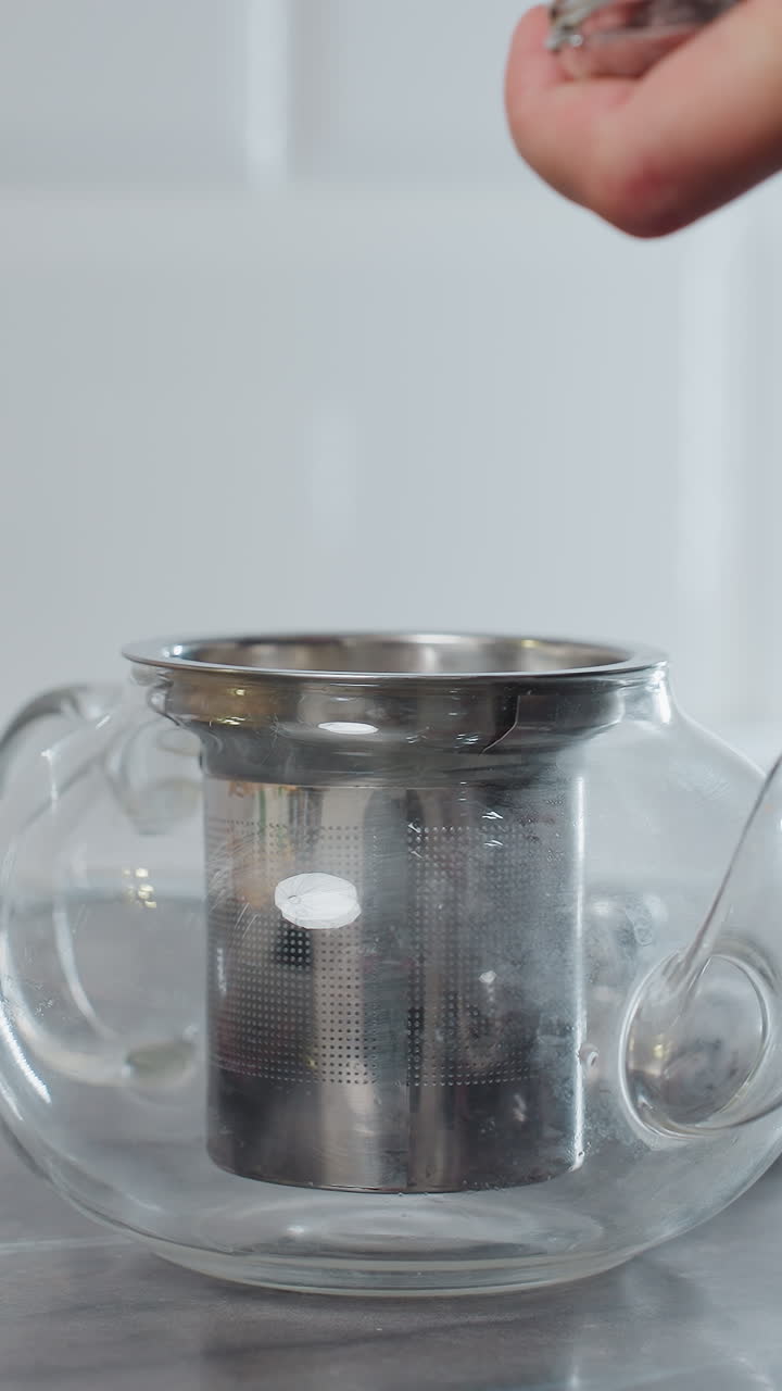 primer plano de una tetera de vidrio con filtro que se llena con sustancia de un paquete, alguna sustancia derramándose sobre la mesa, evocando una atmósfera de cocina hogareña