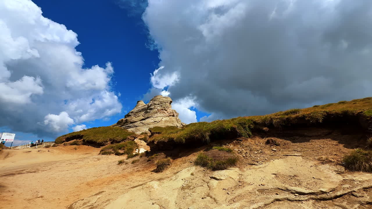Sentiero escursionistico con formazioni rocciose sotto un cielo blu e nuvole. Persone che camminano lungo un sentiero sterrato accanto a colline rocciose sotto un cielo blu con nuvole.