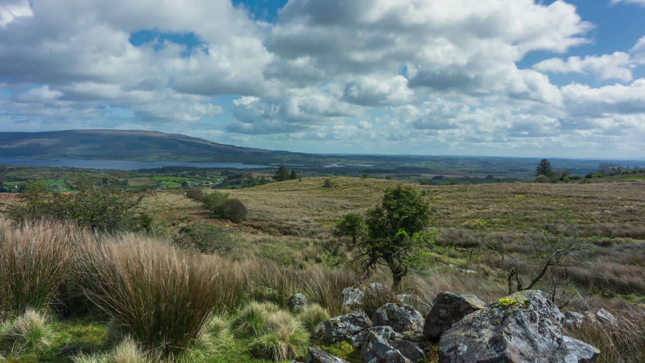 Time lapse of rural landscape with trees in grass and rocky foreground hillside and lake in the distance during a spring sunny cloudy day in Arigna mountains in county Leitrim in Ireland