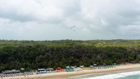 A-La-Izquierda,-Un-Avión-No-Tripulado-De-Un-Camión-Voló-En-Parapente-Sobre-La-Famosa-Playa-Tropical-De-Madeiro-Cerca-De-Pipa,-Brasil,-En-Río-Grande-Do-Norte,-Con-Grandes-Acantilados-Verdes,-Arena-Dorada-Y-Agua-Azul.