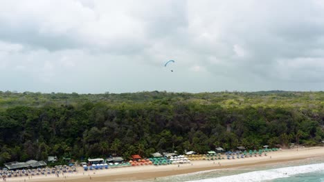 left trucking aerial drone shot de un parapente solitario volando sobre la famosa playa tropical de madeiro cerca de pipa, brasil en río grande do norte con grandes acantilados verdes, arena dorada y agua azul