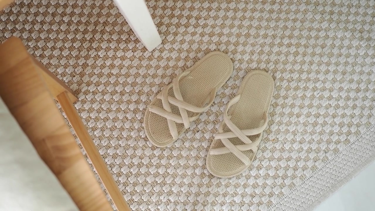 Komfortable beige hjemmesko der hviler på et vævet indendørs tæppe.