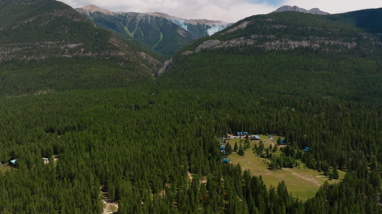 Drone shot panning up to reveal a smoking forest fire in a remote, mountainous area in British Columbia Canada, just outside Kootenay National Park