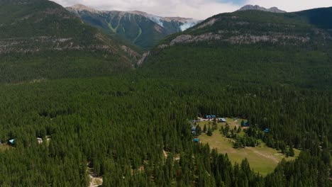 Drone-shot-panning-up-to-reveal-a-smoking-forest-fire-in-a-remote,-mountainous-area-in-British-Columbia-Canada,-just-outside-Kootenay-National-Park