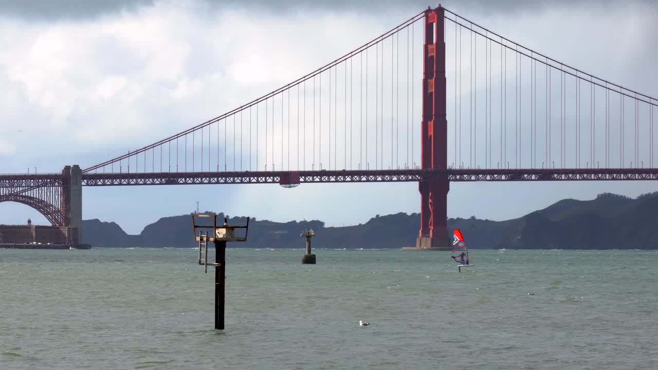 windsurfista distante acelera a través de aguas turbulentas frente al puente golden gate en san francisco