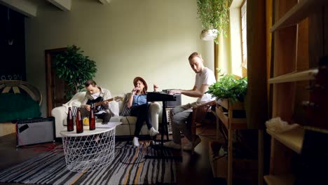 attractive young woman vocalist is singing in microphone while her friends guys are playing the keyboard and the guitar in spacious light home studio.