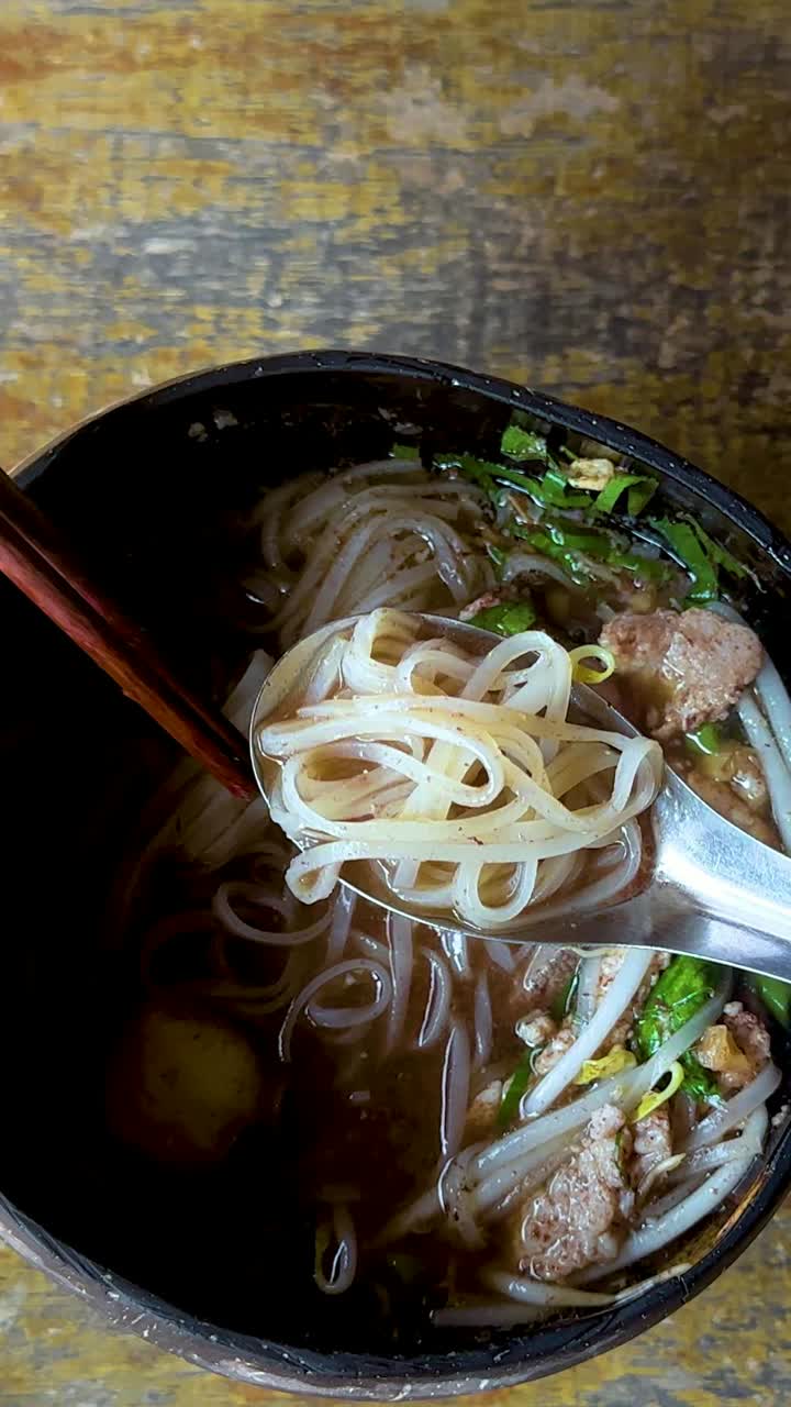 Person enjoying noodles with chopsticks and spoon