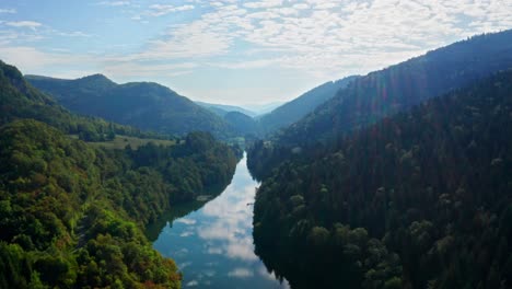 los rayos de sol caen en un río reflectante que corre a través de un paisaje montañoso boscoso, dron aéreo