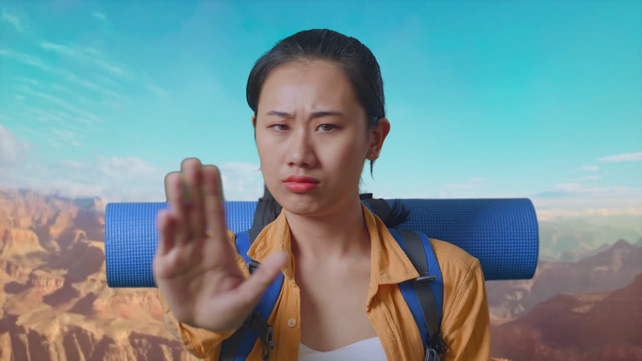 Close Up Of Asian Female Hiker With Mountaineering Backpack Looking At Camera And Making Stop Hand Sign While Traveling At The Top Of Mountain