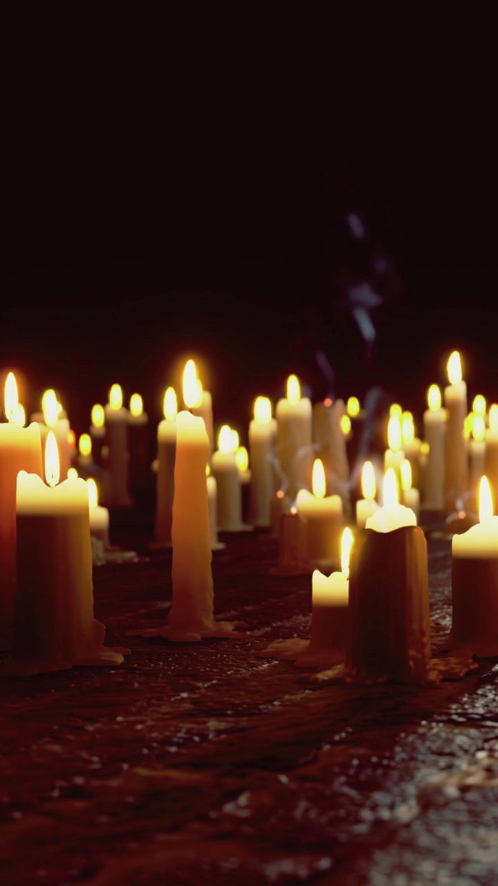 Molte candele accese su una superficie in un ambiente buio di sera.