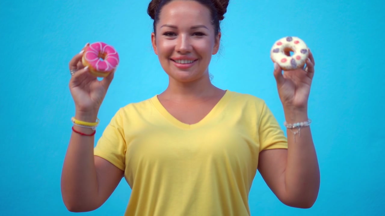 Smiling Woman Holding Two Decorated Donuts Against Blue Background
