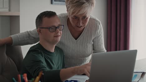 Caucasian man with down syndrome learning with his mum at home.